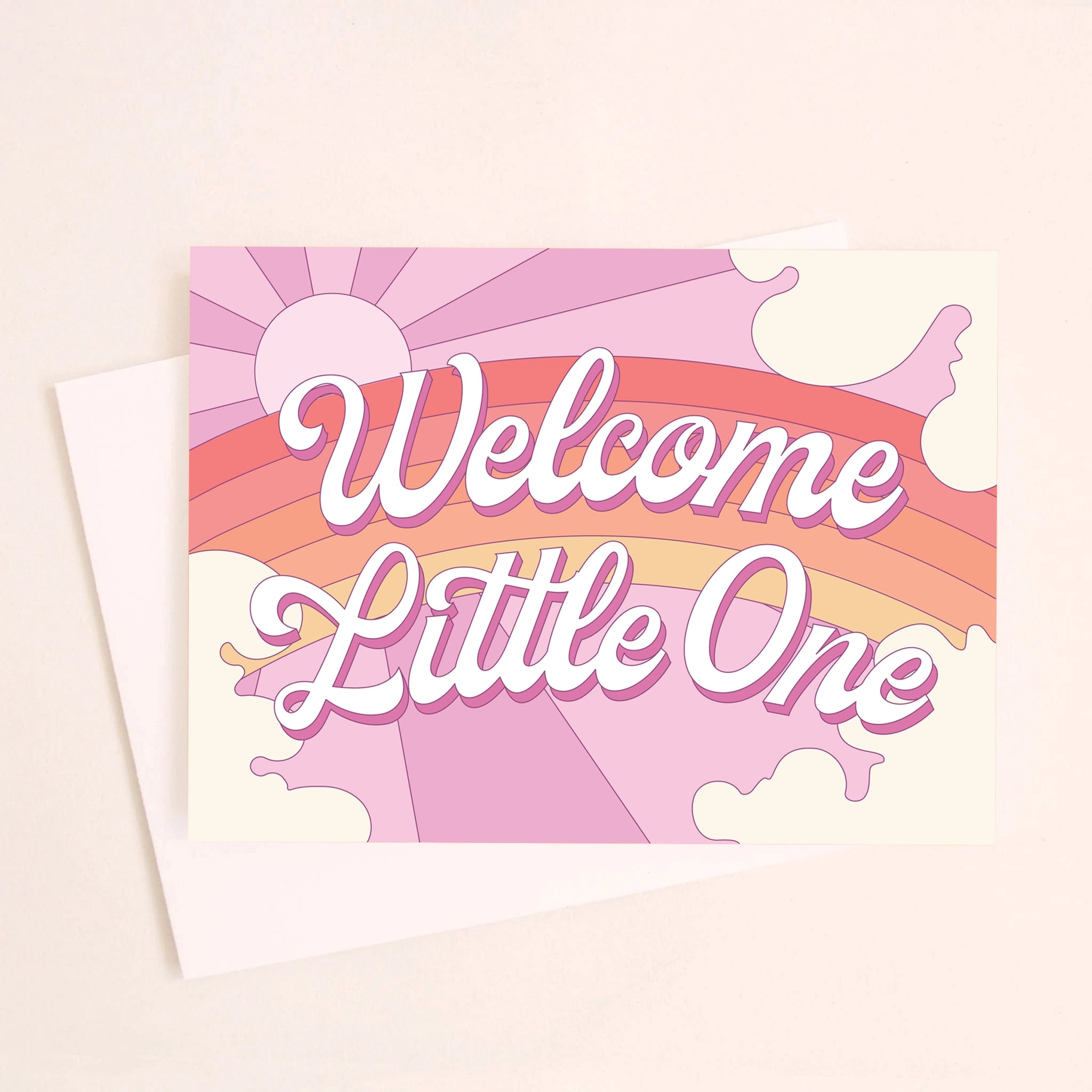 On a light pink background is a greeting card featuring a rainbow and sun graphic and white text in the center that reads, &quot;Welcome Little One&quot;.
