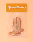 An orange cowboy boot shaped air freshener with a white string for hanging.
