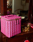 Pink square makeup case with a gold zipper. The makeup case is shown on a vanity.