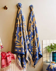 A blue and cream floral pattern bath towel with fringe detailing on two ends.