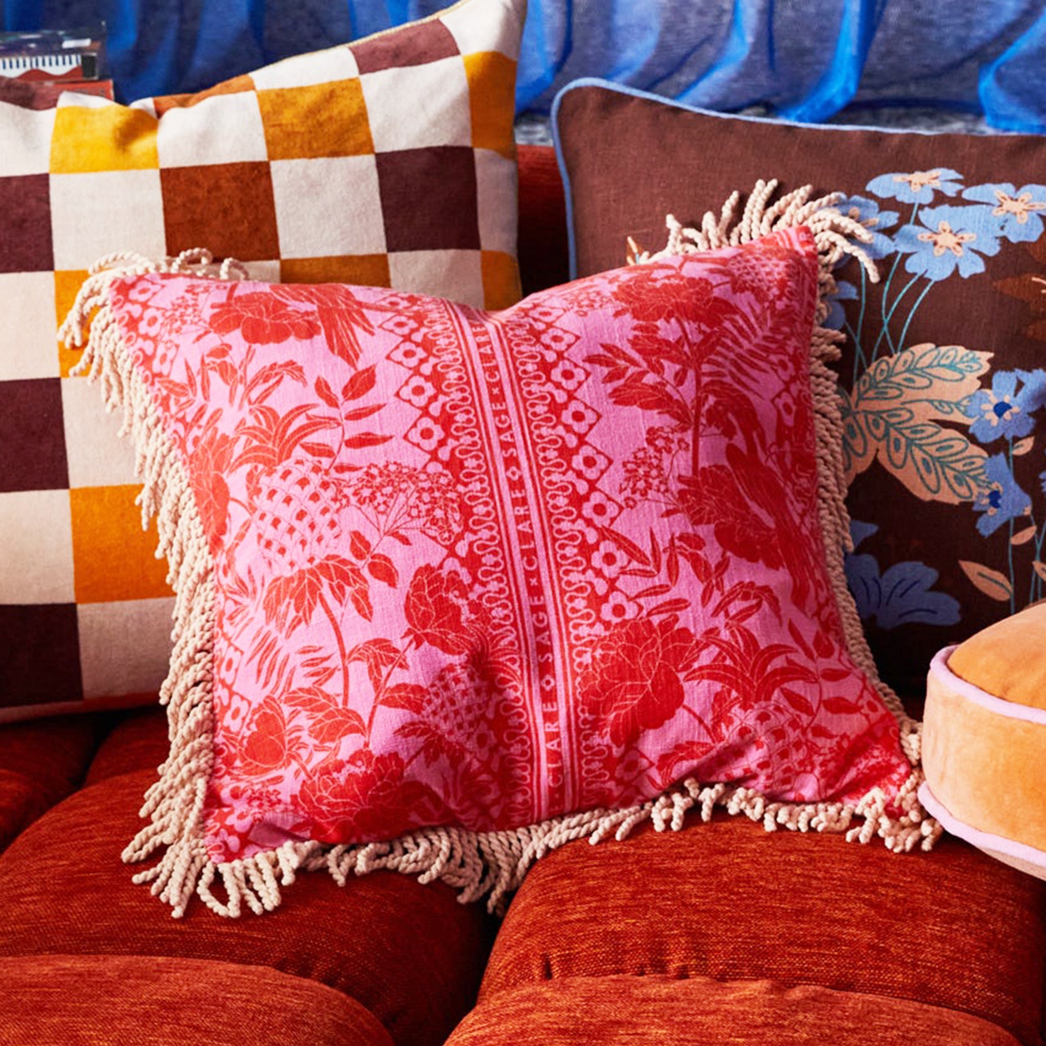 A pink and orange tropical print pillow with a. tassel edge.