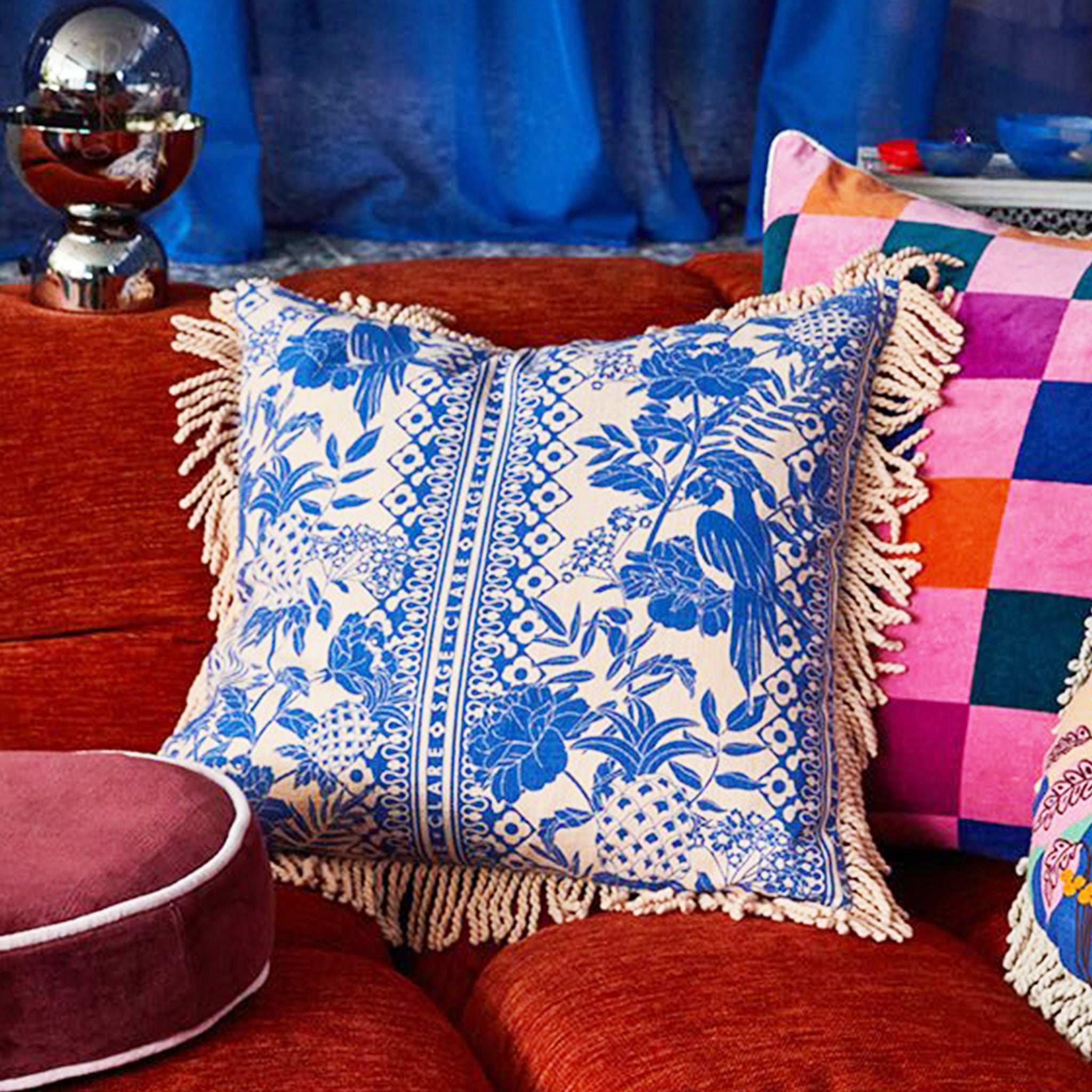A blue and ivory tropical print pillow with a tassel detail along the edges.