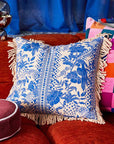 A blue and ivory tropical print pillow with a tassel detail along the edges.