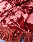 A pink and rust tropical print with "sage x clare" down the side of one edge along with fringe edges on all sides.