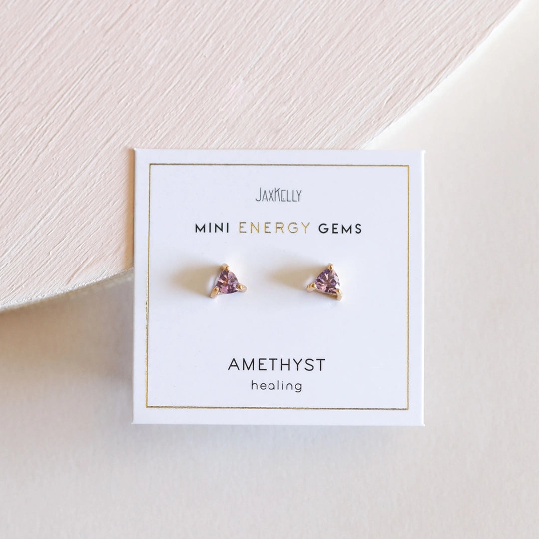 Triangle shaped amethyst set gem on gold stud earrings on white earring card labeled &quot;JaxKelly. Mini Energy Gems. Amethyst. Healing.&quot;