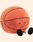 On an orange background is an orange basketball stuffed toy with a smiling face and feet.