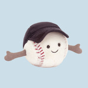 On a white background is a baseball shaped stuffed toy wearing a black baseball cap and a smiling face.