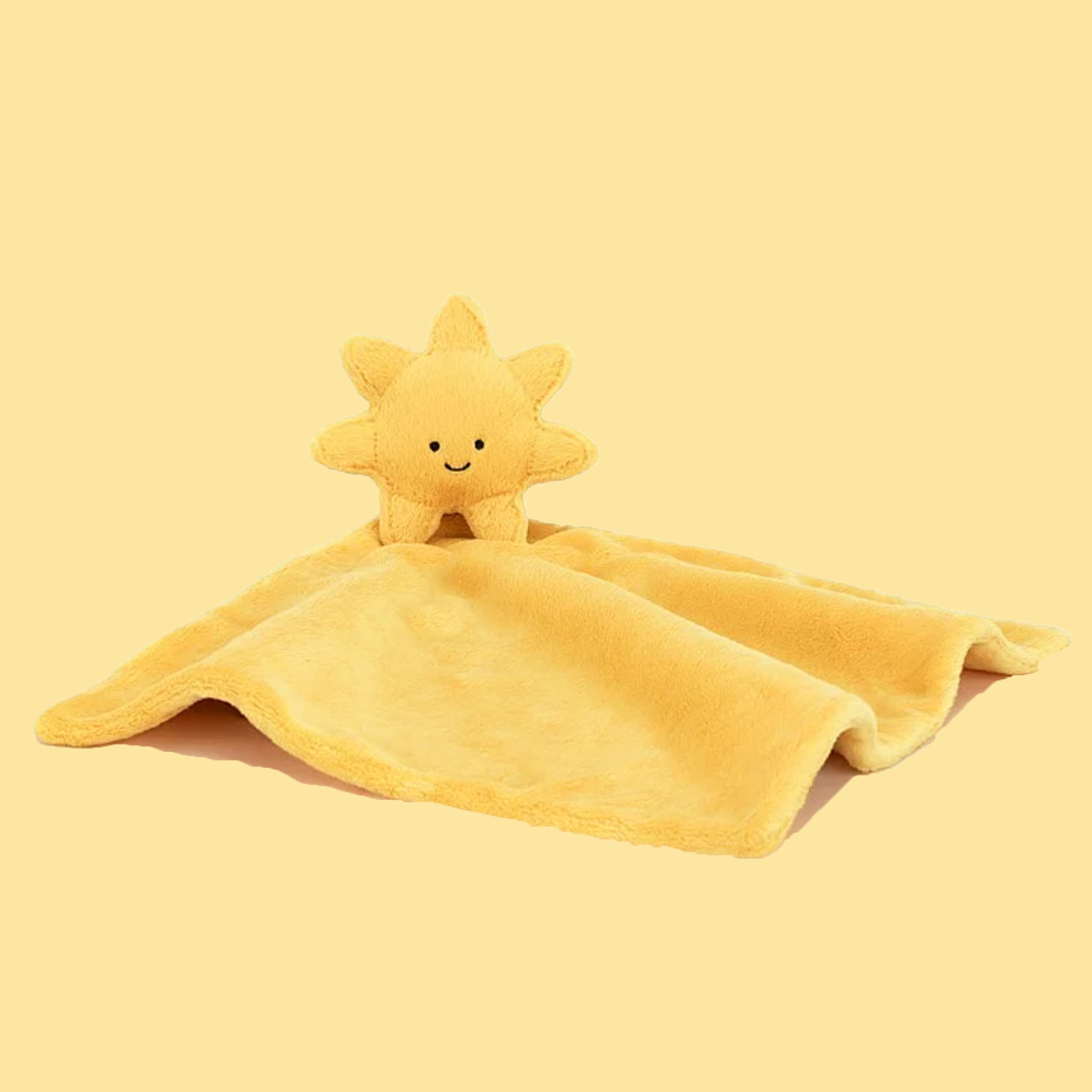 On a yellow background is a yellow sun shaped stuffed toy attached to a square blanket. 