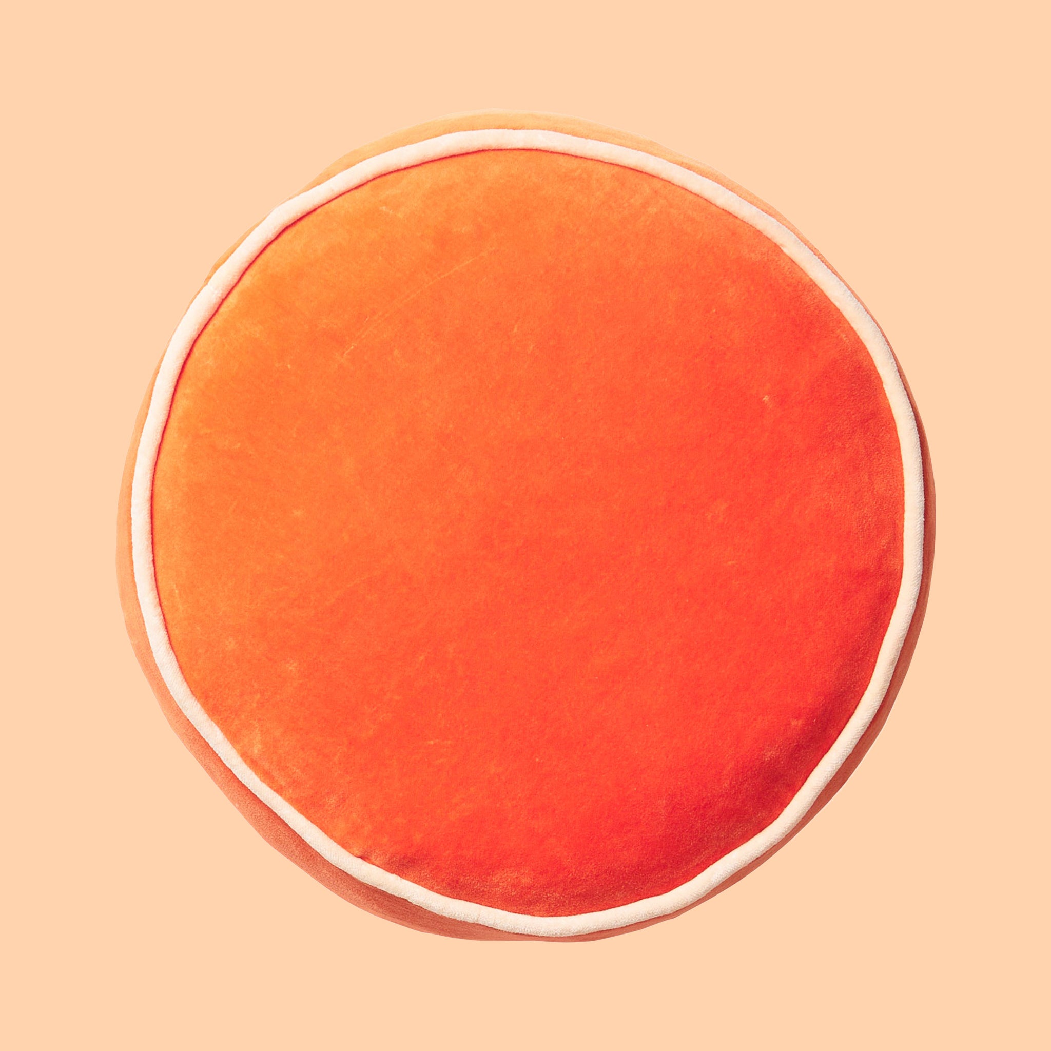 A round orange velvet pillow with an ivory edge. 