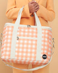 An ivory and apricot checkered print picnic bag with white straps and zippers.