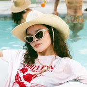 A model wearing a bone colored straw cowboy style hat with a rope neck tie detail.