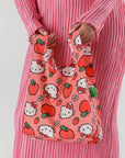 On a white background a model is holding a hello kitty and apple printed nylon tote bag.