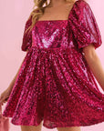 On a pink background is a hot pink sequin romper with puff sleeves and a square neckline.
