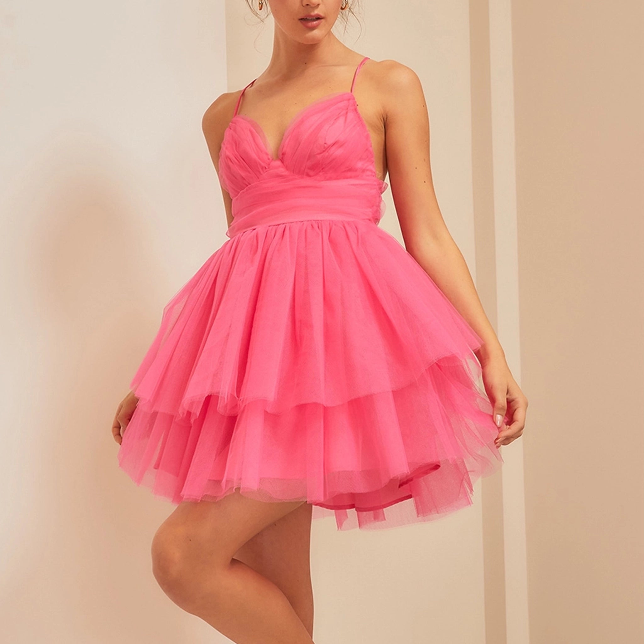 On a neutral background is a model wearing a hot pink tulle mini dress with a sweetheart neckline and thin straps. 