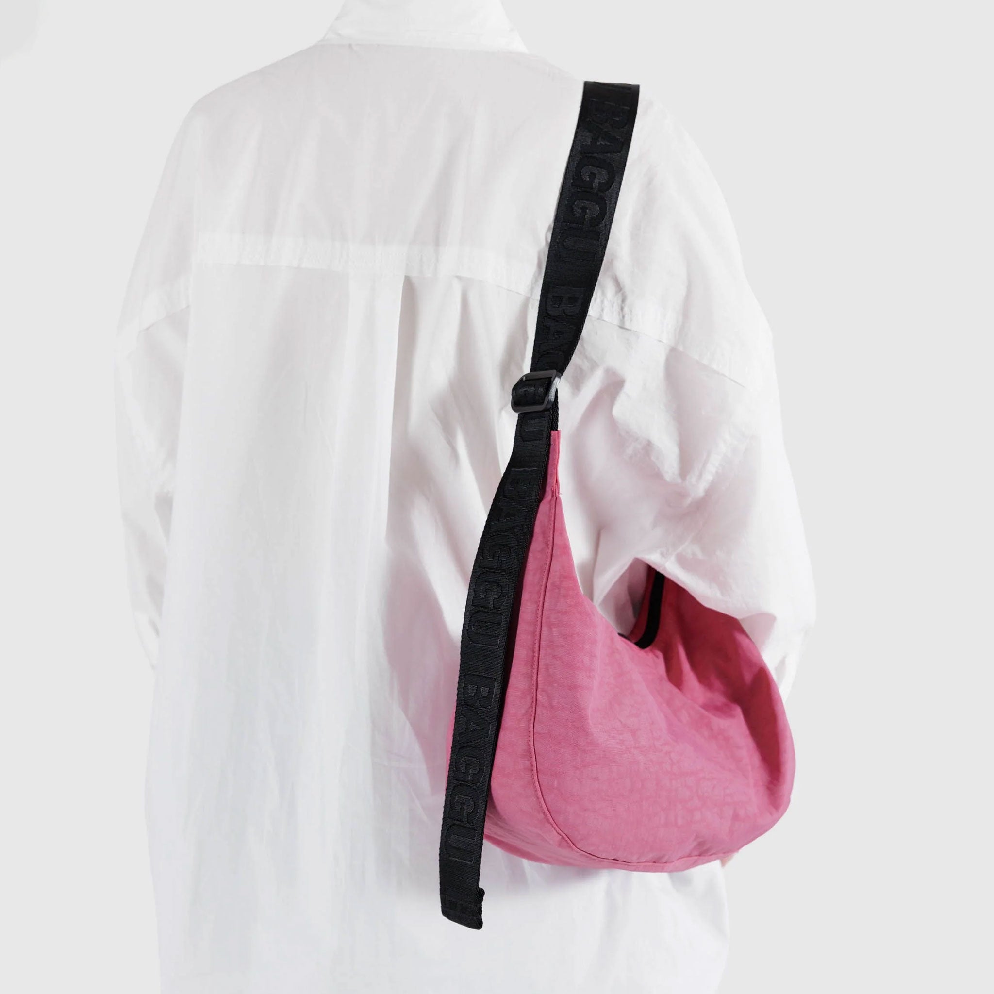 a bright pink crescent shaped bag with black strap