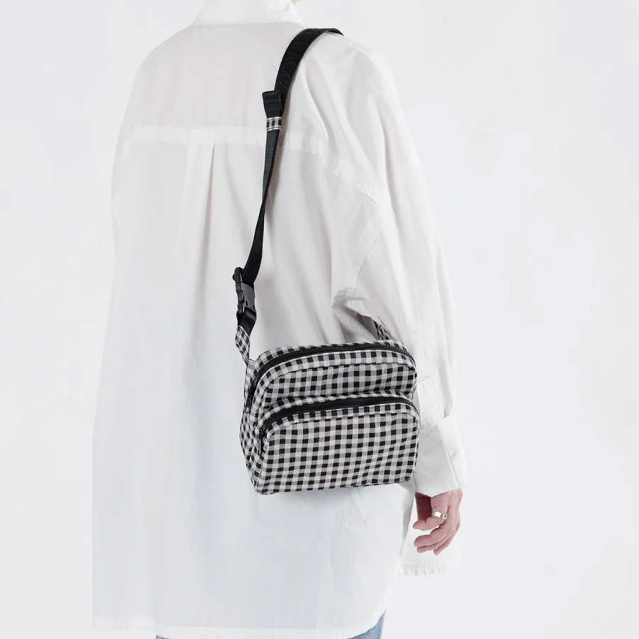 a black and white gingham print fanny pack with black strap hangs off of a person&#39;s shoulder