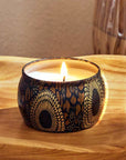 Round tin candle vessel and lid with dark and light gold floral pattern and white wax candle.