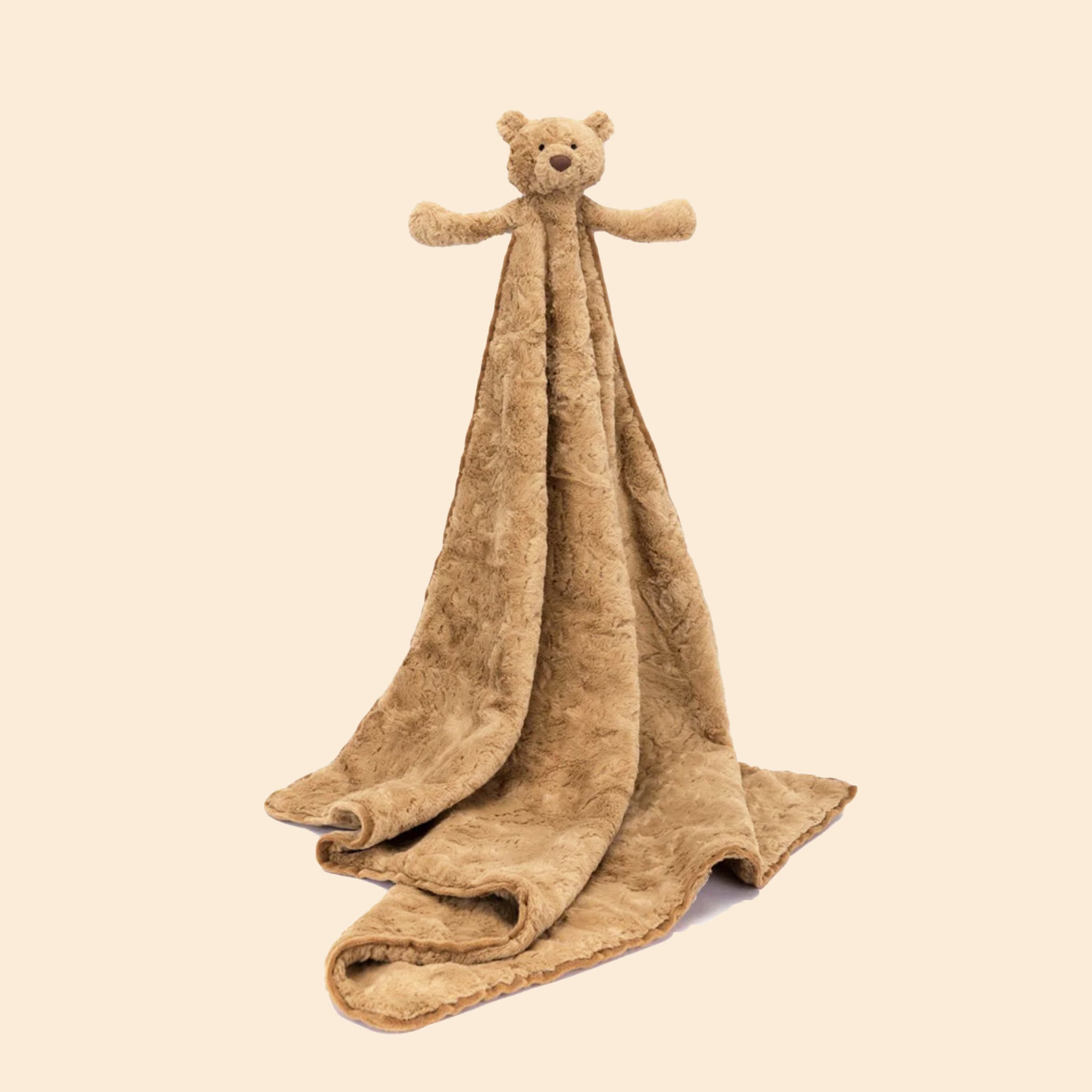 On a tan background is a tan stuffed toy bear attached to a large soft tan blanket. 