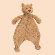 On a tan background is a stuffed toy bear head attached to a furry blanket shaped like a the bear's shape.