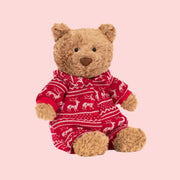 A brown bear stuffed animal wearing a red winter pajama onesie.
