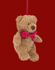 A bear shaped stuffed animal ornament wearing a red bow.