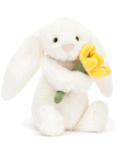 On a white background is a fuzzy white bunny stuffed animal toy with long floppy ears and holding a stuffed daffodil.