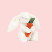 A white stuffed animal bunny holding an orange stuffed carrot.