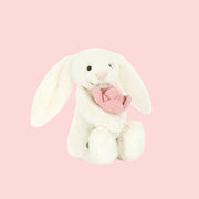 A white bunny shaped stuffed animal holding a pink stuffed toy peony flower.