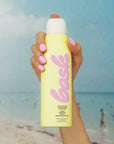 A yellow bottle of spray sunscreen with pink text that reads, "bask".