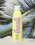 A yellow bottle of spray sunscreen with pink text that reads, "bask".