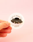 A black speckled bat shaped mini hair clip on a round piece of packaging that reads, 'Let's Hang Sunshine Studios'.