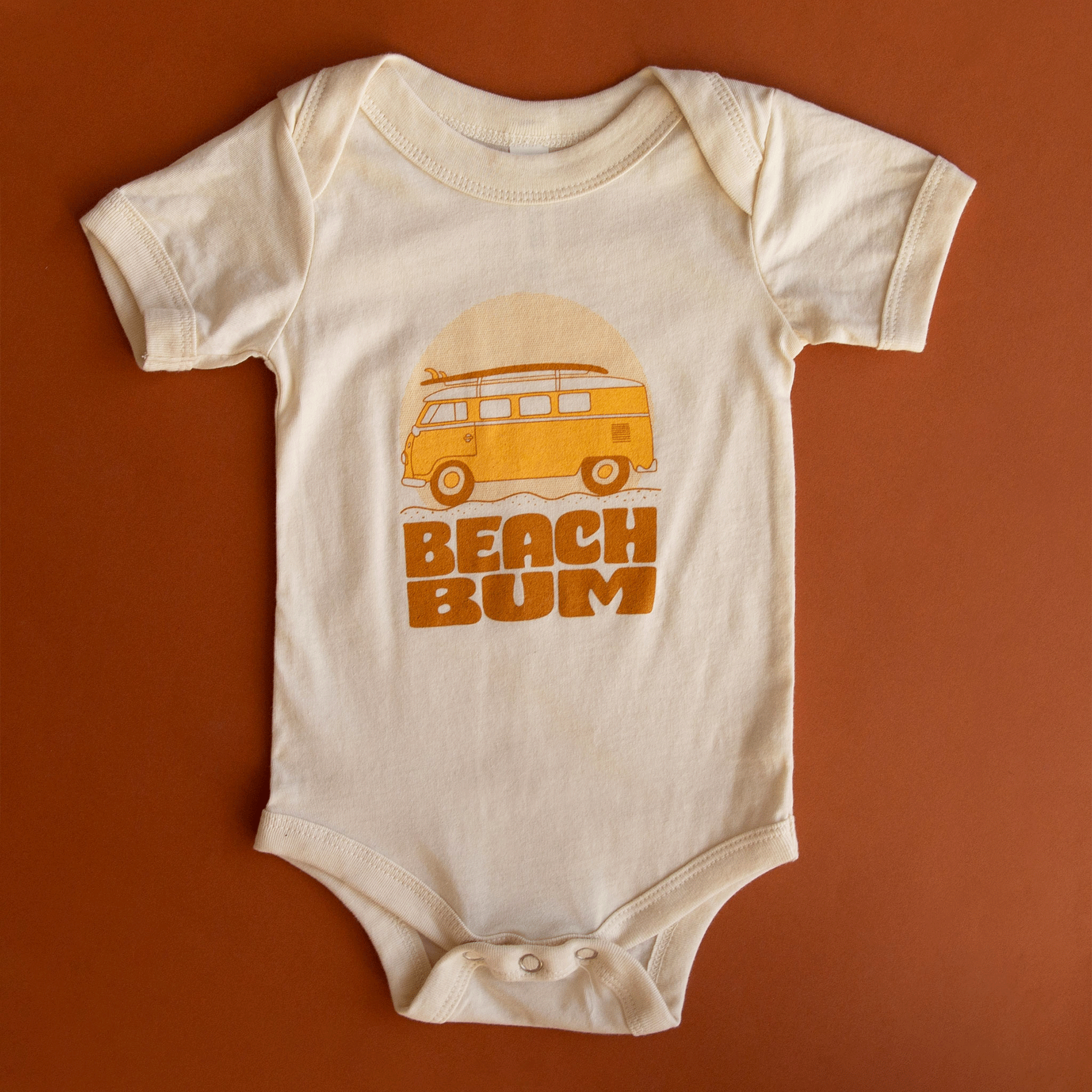 A white cotton onesie with an orange VW bus lined with surfboards and the writing &quot;Beach Bum&quot; in a burnt orange shade.