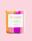 Irridescent pink and orange glass candle with white label that reads, "Beach Vacay". The background of the image is pink.