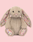 A beige bunny shaped stuffed animal toy with a floral pattern in the ears and on the feet.