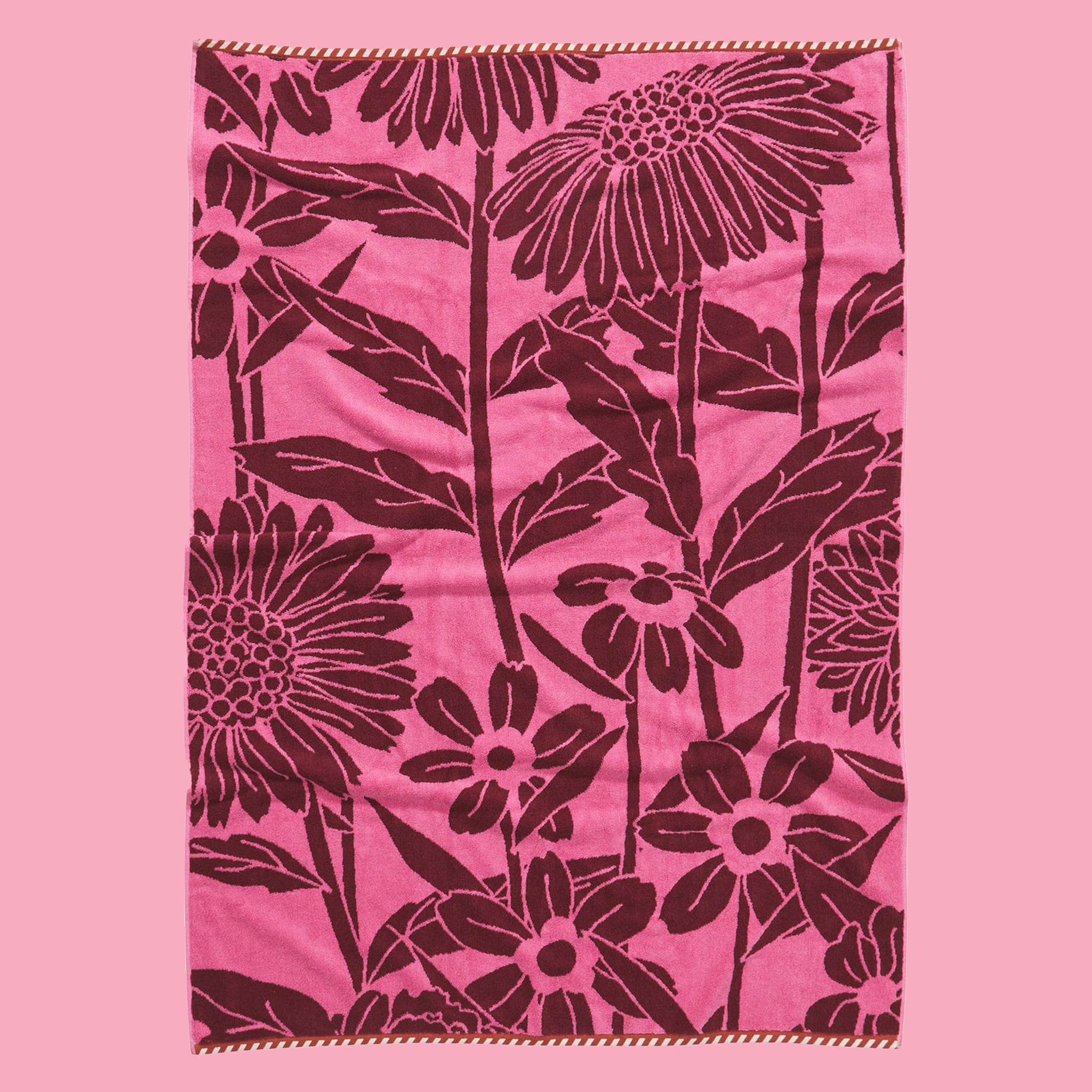 On a pink background is a pink and burgundy floral print bath towel. 
