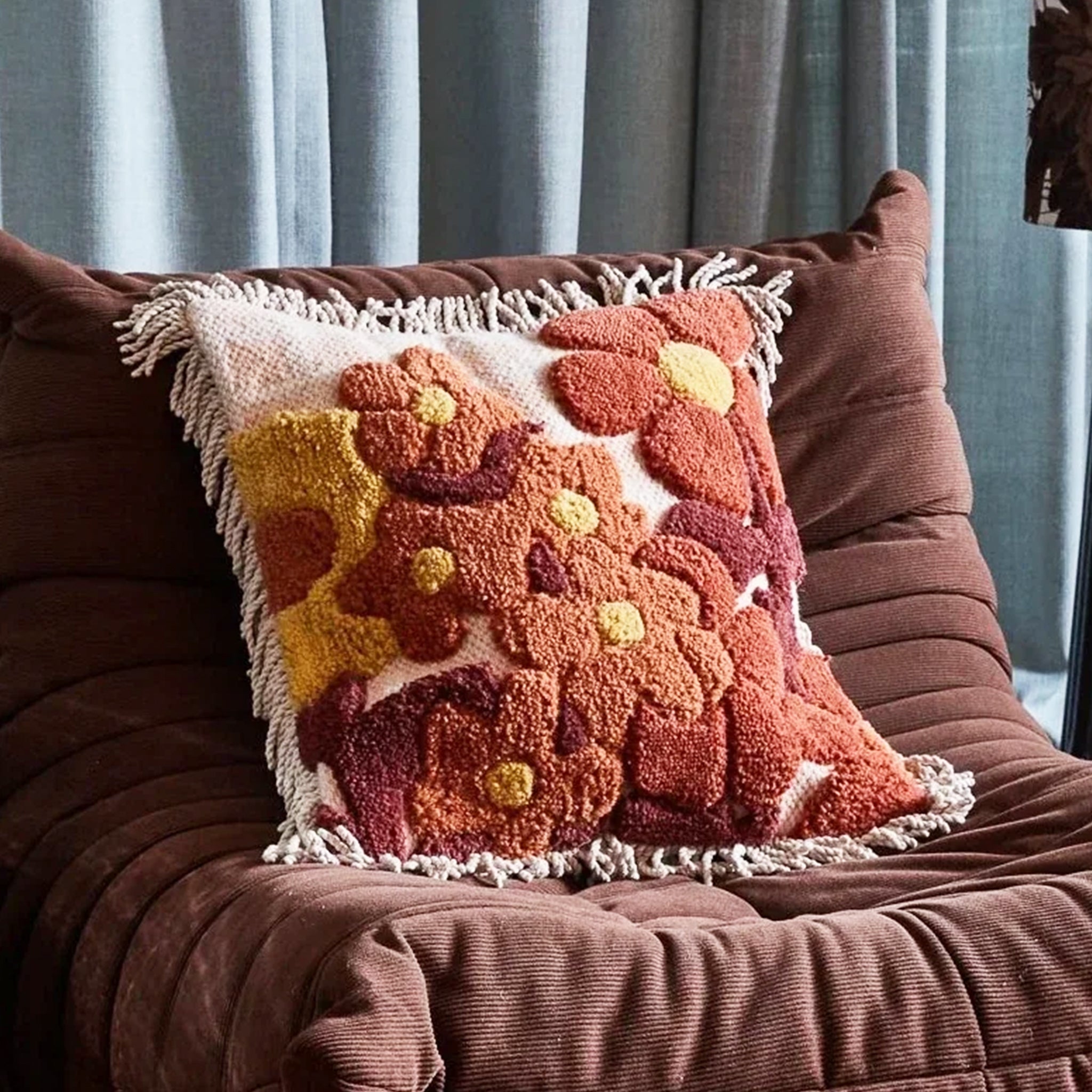 A brown, orange and yellow floral printed pillow with a fringe detail.