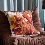 A brown, orange and yellow floral printed pillow with a fringe detail.