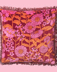 A pink and orange floral printed pillow with a fringe detail.