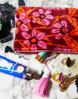 A pink, orange and rust colored floral print velvet pouch with a pink tassel zipper detail.