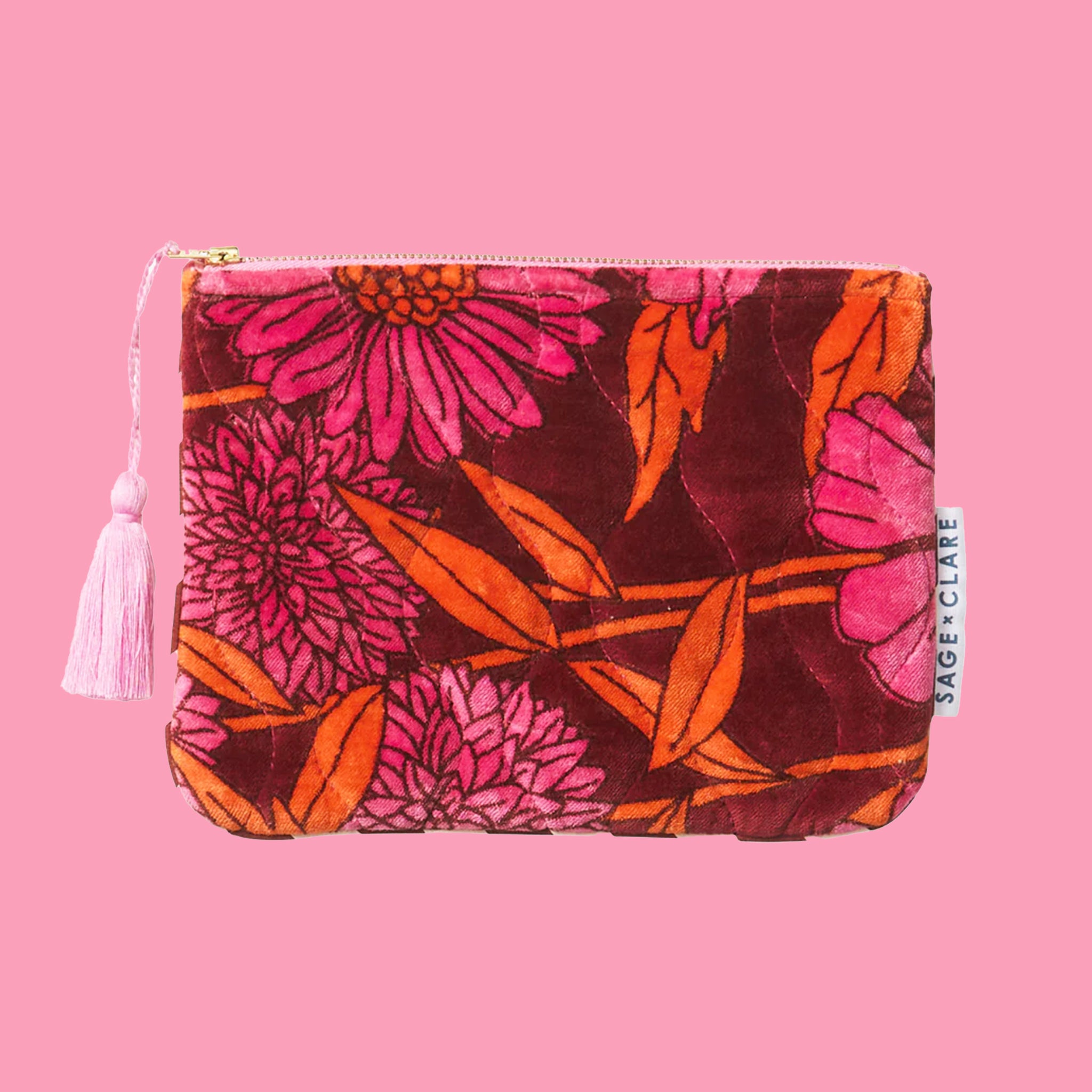 A pink, orange and rust colored floral print velvet pouch with a pink tassel zipper detail. 