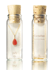 On a white background is a clear glass bottle with a cork top and filled with a gold chain necklace with a teardrop shaped carnelian July birthstone.