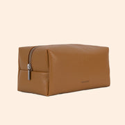 A warm brown vegan leather toiletry / cosmetic bag with a zipper closure and handle on one side.