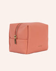 A coral vegan leather toiletry case with a handle on one side and a zipper closure across the top.
