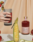 A glass bottle of bloody mary mix with a pink label and a gold lid.