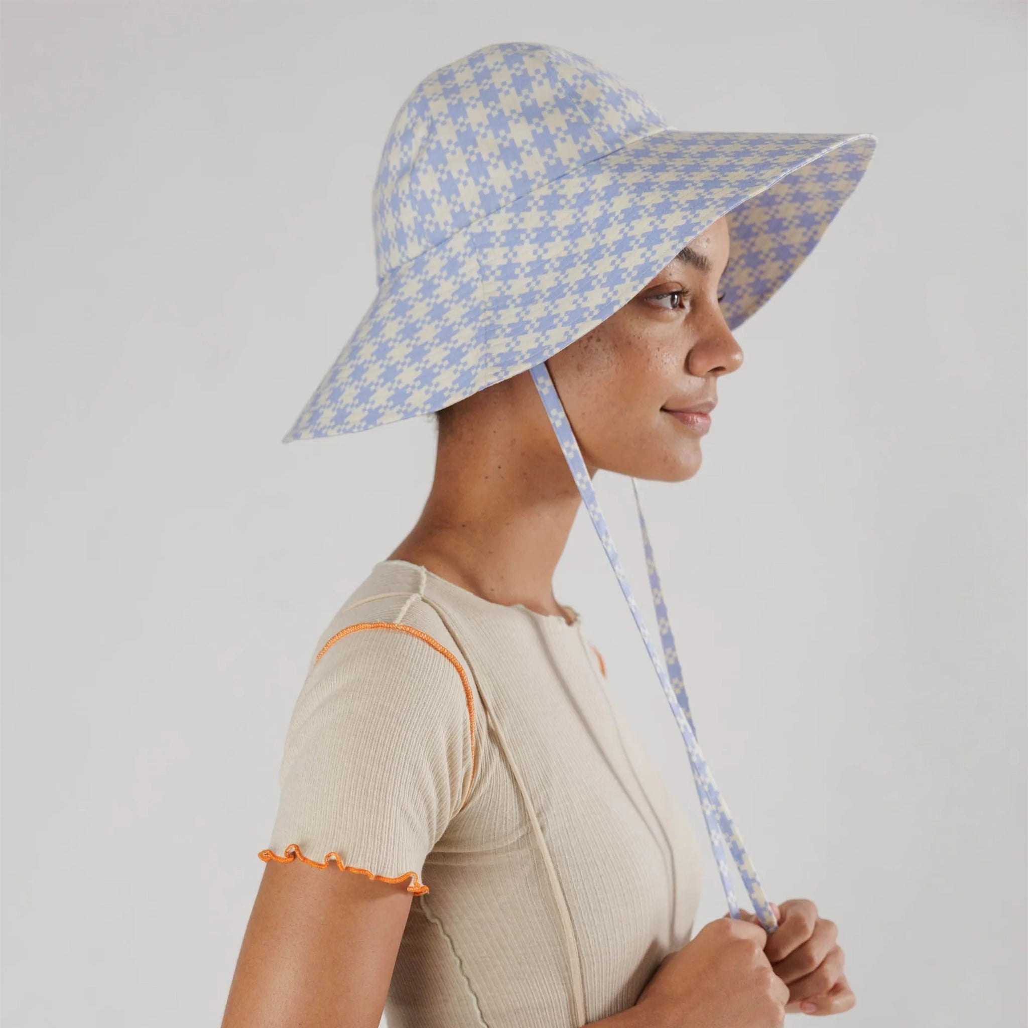 On a white background is a flexible sun hat with straps for securing around the neck with a blue and white gingham print. 