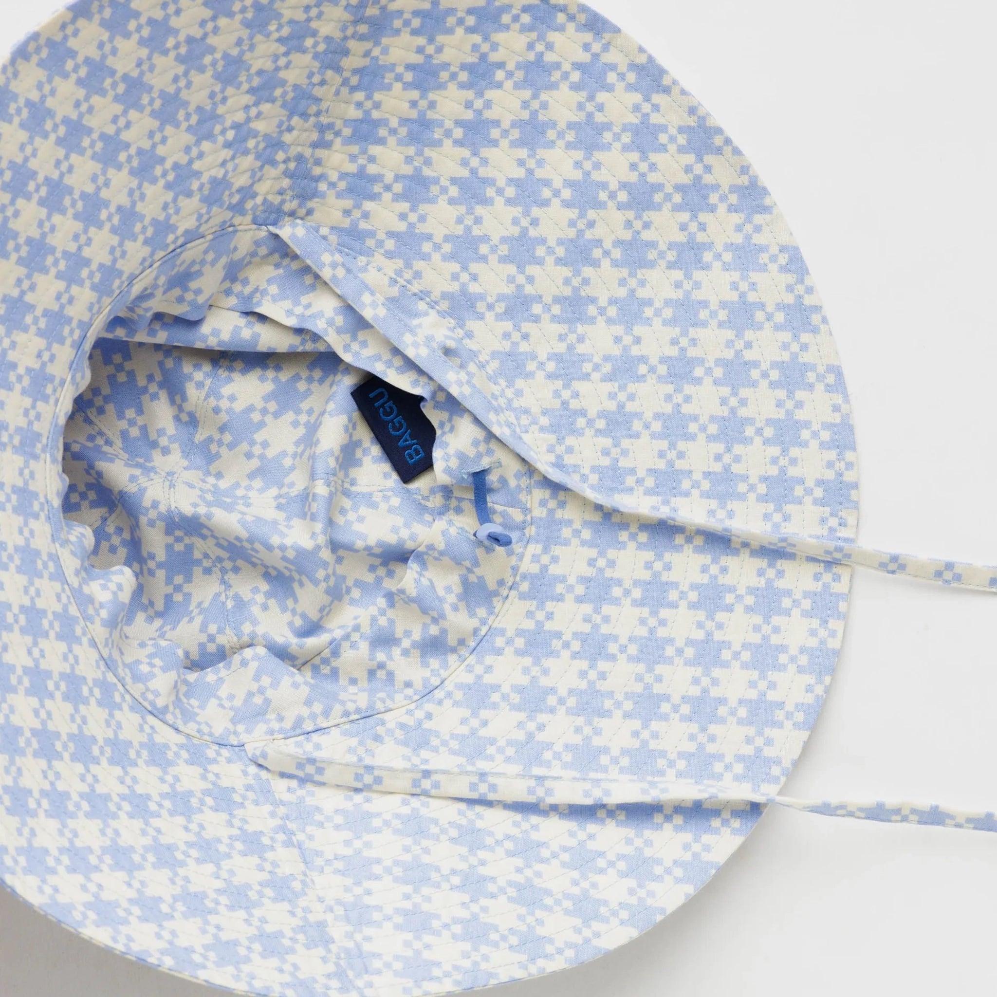 On a white background is a flexible sun hat with straps for securing around the neck with a blue and white gingham print.