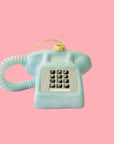 A blue rotary phone ornament on a pink background.