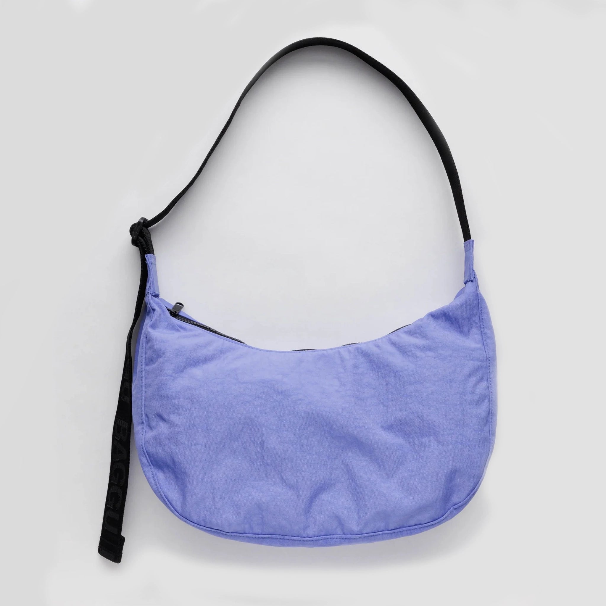 On a white background is a blue crescent handbag with black accents and a black over the shoulder strap. 