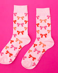 A pair of light pink socks with red, orange and pink bow patterns all over.