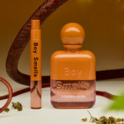 An orange and clear bottle of perfume with text that reads, 'Cowboy Kush' along with a travel spray next to it.